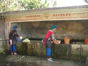 ...beim Dorfbrunnen auf Gemuese waschende Frauen in ihrer traditionellen Tracht...